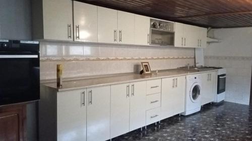 cocina con armarios blancos, lavadora y secadora en Casuta de sub munte, en Buzau