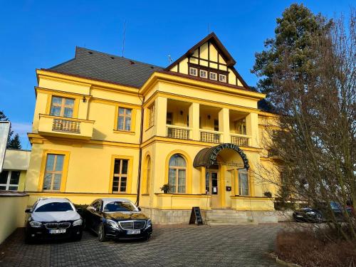 two cars parked in front of a yellow house at Palace Inn in Jíloviště
