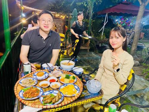 Ein Mann und eine Frau sitzen an einem Tisch mit Essen in der Unterkunft Wooden Homestay Đại Lải in Phúc Yên