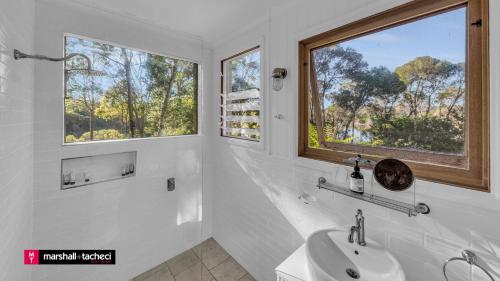 une salle de bain blanche avec un lavabo et deux fenêtres dans l'établissement Bermagui Jewel on the Lake Cuttagee Bermagui Wifi provided, à Bermagui