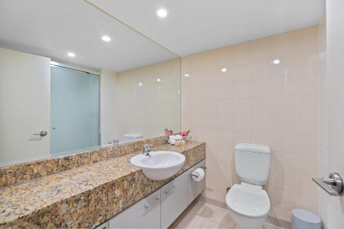 a bathroom with a sink and a toilet and a mirror at Belle Escapes Drift Beachfront Resort Pool View Suite 4106 in Palm Cove