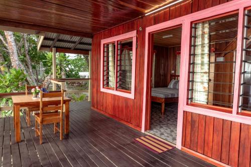 ein rotes Haus mit einer Holzterrasse mit einem Tisch in der Unterkunft Leleana Resort Kolombangara Island 