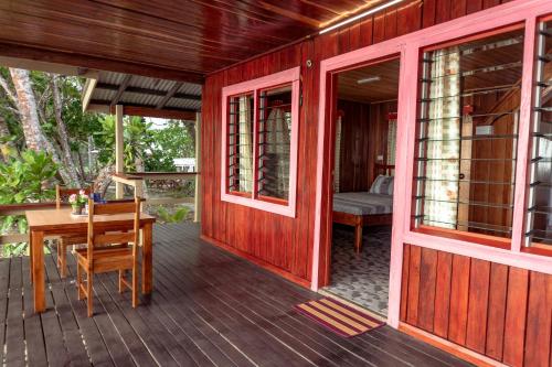 Kolombangara IslandLeleana Resort Kolombangara的红色的房子,设有木甲板和桌子