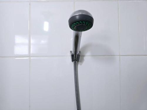 un pommeau de douche sur un mur carrelé blanc dans l'établissement Apt Bassura Studio Tower F w/ Pool, Wi-Fi & Netflx, à Jakarta