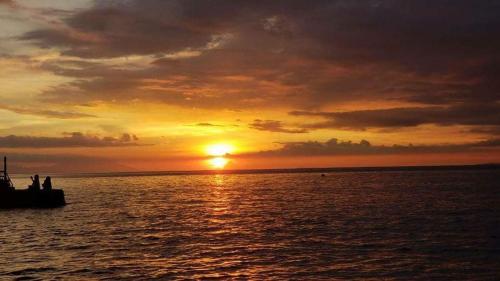 Dive and Trek Resort and Marine Sanctuary في Bauan: غروب الشمس على هيئة ماء مع قارب