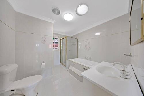 Baño blanco con lavabo y aseo en Discover Mount Annan - Spacious 6-BR House, en Narellan