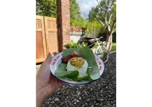 a person holding a plate of food on a banana leaf at Yukke Tembi Homestay in Yogyakarta