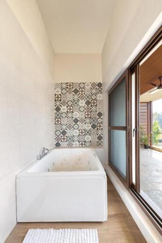 eine weiße Badewanne in einem Zimmer mit Fenster in der Unterkunft Melhor Stays Villa - Mayberry 1BHK in Arpora