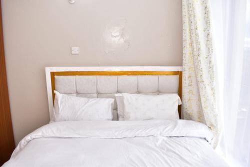 - un lit avec des draps et des oreillers blancs à côté d'une fenêtre dans l'établissement Meshivon suite, à Nairobi