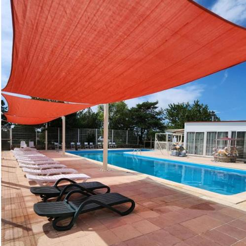 - une piscine avec des chaises longues et un grand parasol rouge dans l'établissement CAMPING / LOCATION MOBIL HOME : Les gorges du Verdon et lac de Sainte Croix., à Sainte-Croix-de-Verdon