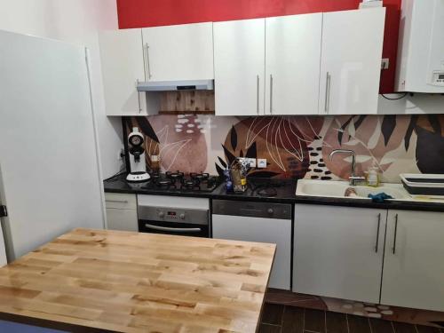 une cuisine avec des armoires blanches et une table en bois dans l'établissement L’Oasis Fleuri, à Bourg-de-Péage