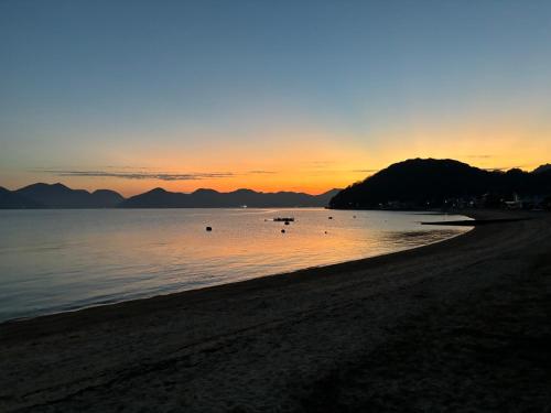 a sunset on a beach with mountains in the background at East Villa Shimanami Mukaishima seafront in Onomichi