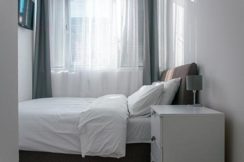 ein Bett mit weißer Bettwäsche und Kissen neben einem Fenster in der Unterkunft One-Bedroom Apartment in the Center of Budva on a Quiet Street 5 Minutes to the Beach in Budva