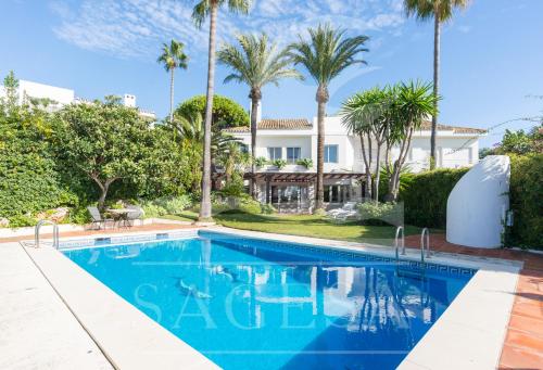 a swimming pool in front of a house with palm trees at Jardines de las Golondrinas in Marbella