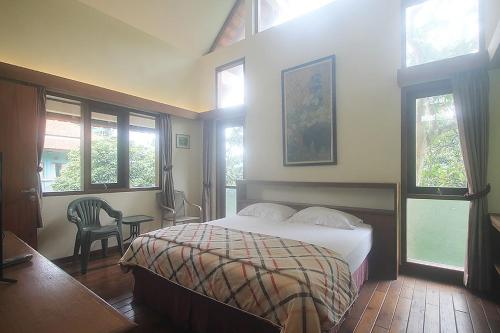 a bedroom with a bed and a chair and windows at Hotel Villa Rawa Pening Pratama by Aparian in Bandungan