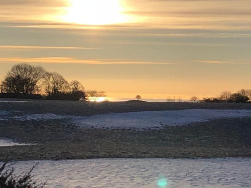 um campo coberto de neve com o sol no céu em Sagolikt läge med havsutsikt i Rörum på Österlen em Simrishamn