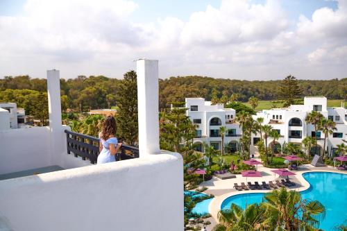 a woman standing on a balcony looking at the pool at a resort at Pullman Mazagan Royal Golf & Spa in El Jadida