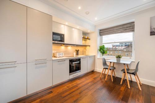 a kitchen with white cabinets and a table with chairs at Luxury One Bedroom Apartment With AC, Bidet, Balcony View, Free Coffee, Tea, WiFi in Central London in London