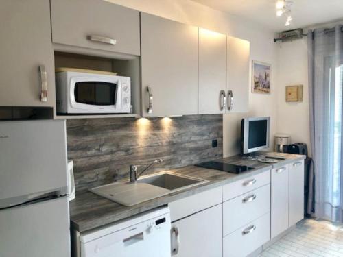 une cuisine avec des armoires blanches, un évier et un micro-ondes dans l'établissement Villa 41, Port Vénus au village naturiste, au Cap d'Agde