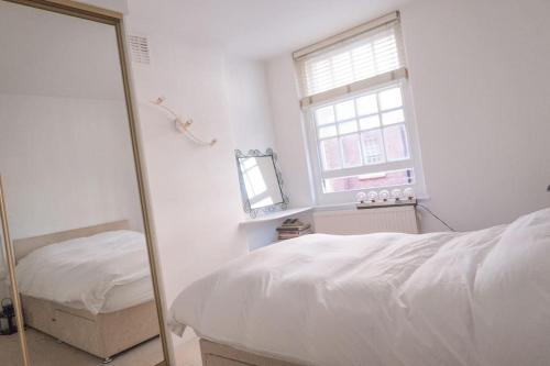 a mirror in a bedroom with a bed and a window at Bright wood-floor apartment near Parliament in London