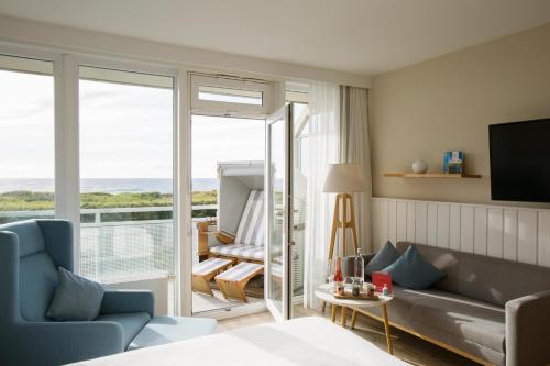 a room with a bed and a couch and a balcony at Wyn. Strandhotel Sylt in Westerland