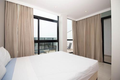 - une chambre avec un lit blanc et de grandes fenêtres dans l'établissement Duplex Luxo Hotel Athos Bulcão Brasília - Ozped Flats, à Brasilia