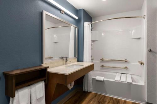 a bathroom with a sink and a tub and a mirror at WoodSpring Suites Yorktown Newport News in Newport News