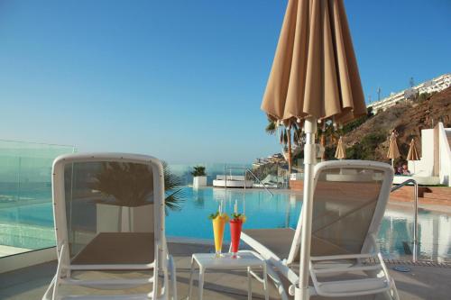 two chairs and an umbrella next to a swimming pool at Servatur Hartaguna - Adults Only in Puerto Rico de Gran Canaria