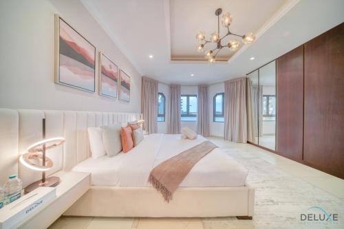 a white bedroom with a large bed and a chandelier at Seaside 5BR Villa with Assistant's Room and Beach Access on Palm Jumeirah by Deluxe Holiday Homes in Dubai
