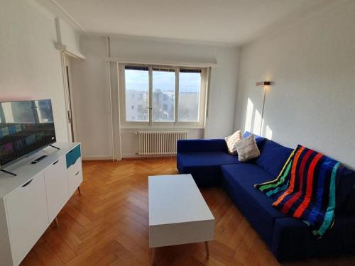Appartement élégant & ensoleillé في لوزان: غرفة معيشة مع أريكة زرقاء وتلفزيون