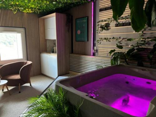 a bathroom with a purple bath tub with a chair at L'appart'hôtel 23ème avenue - Spa privatif - Love room - Appartements à thèmes in Lamalou-les-Bains
