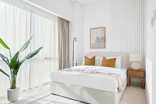 ein weißes Schlafzimmer mit einem großen Bett und einer Pflanze in der Unterkunft Silkhaus Luxury Studio in a Residential Neighborhood in Dubai