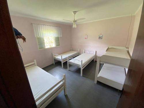 Cette chambre comprend 3 lits, une table et une fenêtre. dans l'établissement Chácara Recanto Solar, à Águas de Lindóia
