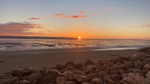 a sunset over the ocean with rocks on the beach at Aux Trois Jean in Le Crotoy
