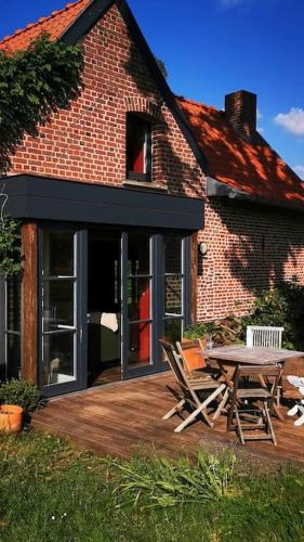 Cette maison en briques dispose d'une terrasse avec une table et des chaises. dans l'établissement ferme de caractère avec piscine et cheminée, à Sainghin-en-Mélantois