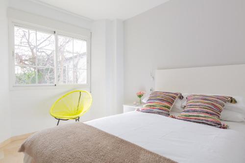 a white bedroom with a bed and a yellow chair at OceanVibe Loft MalagaFlat in Málaga