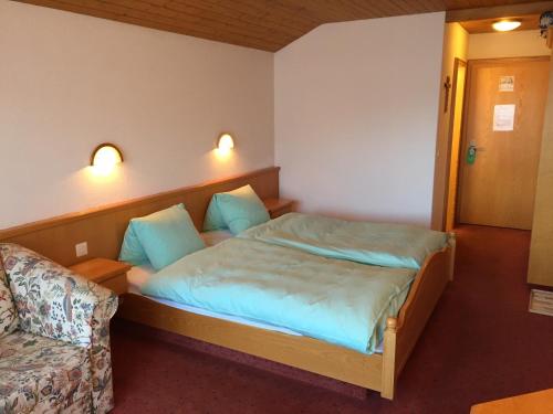 a bedroom with a bed with blue sheets and a chair at Hotel Restaurant Rothorn in Visperterminen
