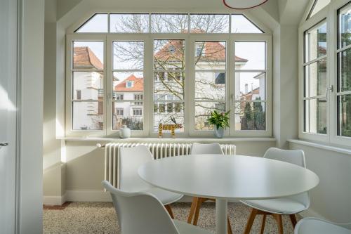 une table et des chaises blanches dans une chambre avec fenêtres dans l'établissement Le cocon d'Emma, terrasse, jardin et élégance dans maison de Maître, à Strasbourg