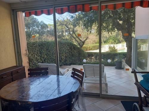 uma mesa e cadeiras em uma sala com uma grande janela em Les Hauts du Golf Rez de jardin Piscine Tennis em Saint-Raphaël
