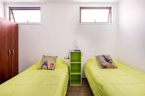 two beds in a room with green sheets and windows at Habitaciones Valparaiso in Valparaíso