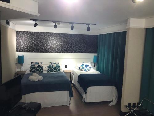 a hotel room with two beds and blue curtains at Quarto de hotel entre os Shoppings Vila Olimpia e JK Iguatemi in Sao Paulo