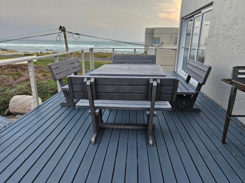 a wooden table and chairs on a deck with the beach at Engel in Struisbaai