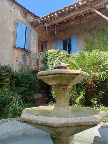 a bird sitting in a fountain in front of a house at Gite Les Volets Bleus du Segur in Le Ségur-Suech