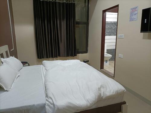 a bedroom with a bed with white sheets and a window at OYO IAE566 Neelkanth Hotel in Rewāri