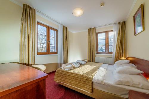 a bedroom with a bed and a desk and windows at Le Mont Medical & SPA in Świeradów-Zdrój