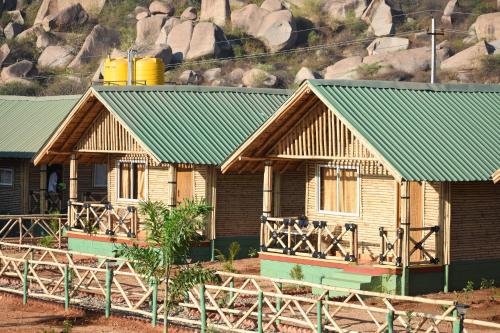 two wooden houses with green roofs in front of a mountain at Mowgli's Cafe Hampi & Guest House in Hampi