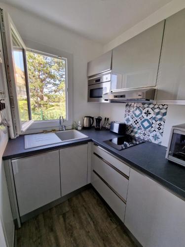 une cuisine avec des armoires blanches, un évier et une fenêtre dans l'établissement Rez-de-jardin bord de mer, à Cabourg