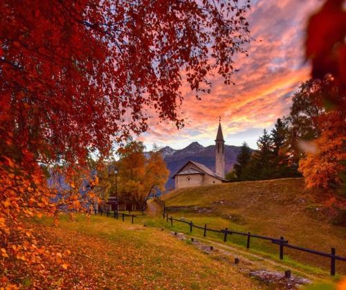a church on a hill with autumn leaves and a fence at THE LITTLE NEST in Valdisotto