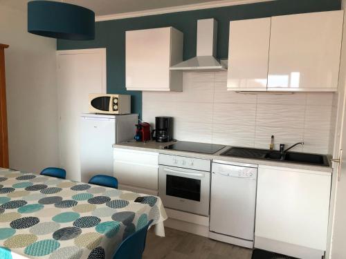 une cuisine avec des placards blancs et une table avec un chiffon de table dans l'établissement LES BALCONS ROUGES - VUE MER, à Sainte-Cécile-Plage
