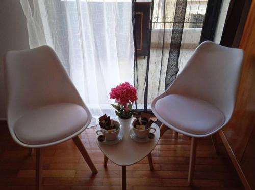 2 weiße Stühle und ein Tisch mit Blumen und einem Fenster in der Unterkunft Nicko’s room in Piräus